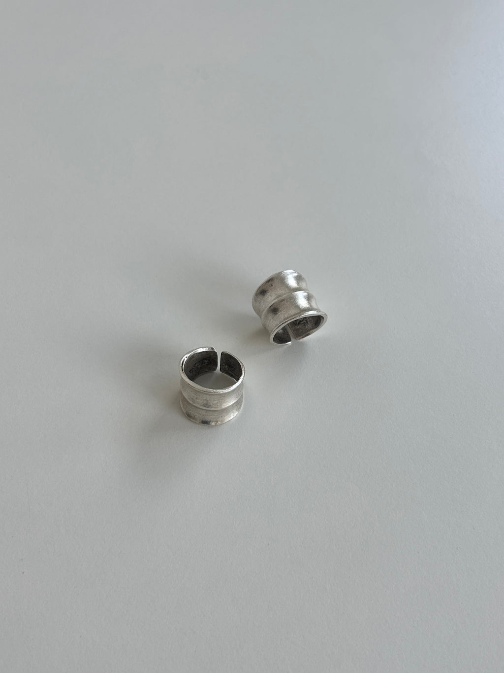Two small silver-toned metal ring-like accessories with a split circular shape, photographed on a plain light gray surface.