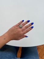 A close-up of a person's hand with bright blue nail polish wearing a wide silver ring with black diagonal stripes, resting on a white table.